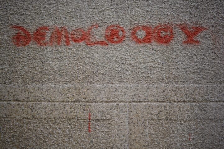 Red graffiti on white pavement which spells the word "DEMOCRACY".