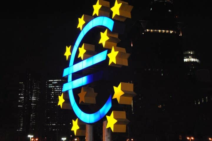 A bright neon sign of a Euro in blue, surrounded by yellow stars.