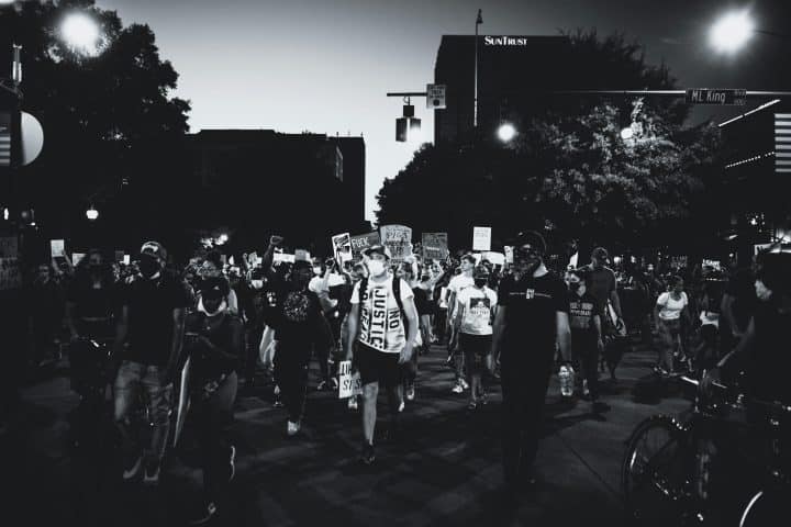 Black and white image of protesters marching down Martin Luther King Boulevard. Many have signs denouncing the police in America; most are wearing face masks.