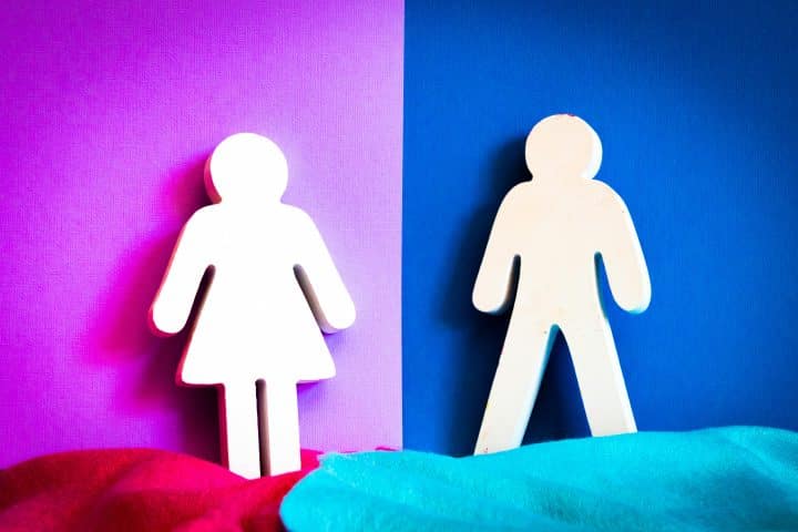 A cutout of a woman, leaning on a pink wall, and a cutout of a man, leaning on a blue wall.