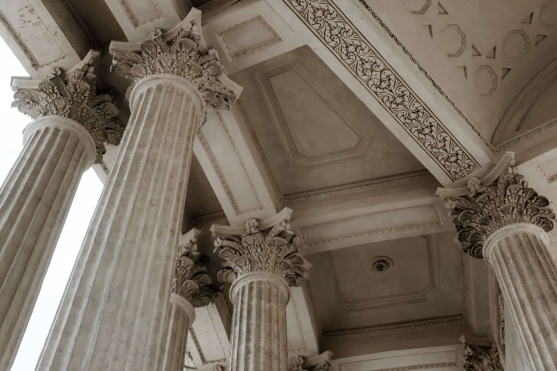 The ceiling of a building is shown, built in a classical fashion which mimics the architecture of the ancient Greeks, with tall columns holding up the roof.