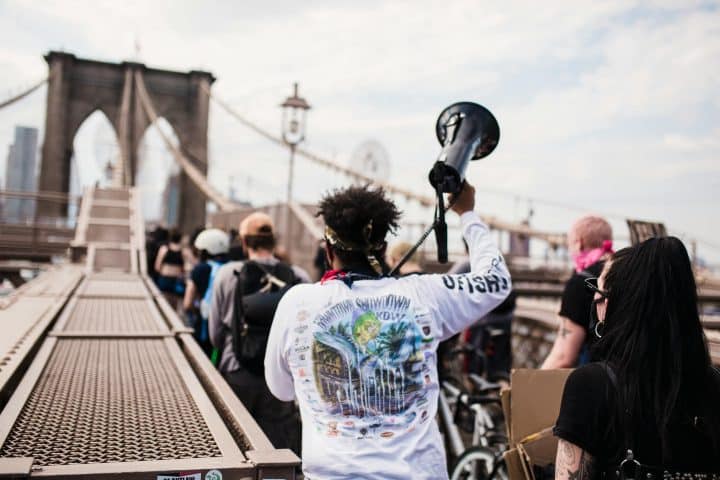 Protestors walking down Brooklyn bridge, one holding aloft a megaphone.