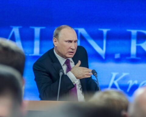 Rysslands President Vladimir Putin talar på en scen med två mikrofoner framför sig.