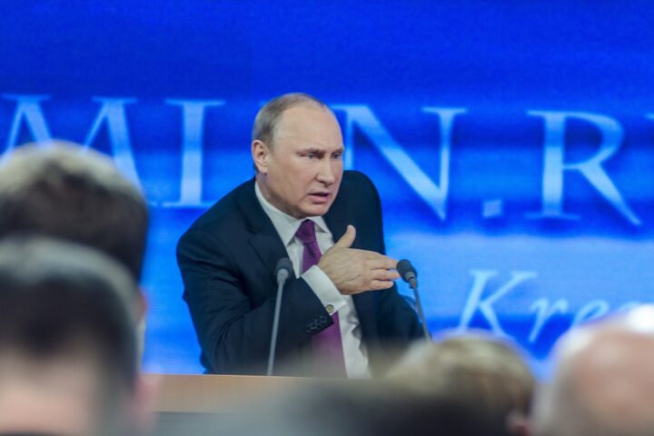 Rysslands President Vladimir Putin talar på en scen med två mikrofoner framför sig.