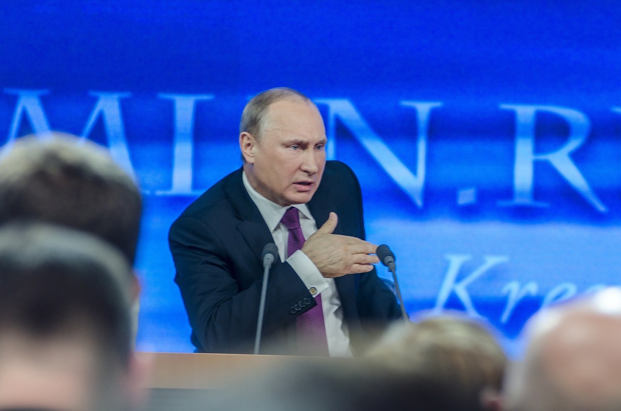 Rysslands President Vladimir Putin talar på en scen med två mikrofoner framför sig.