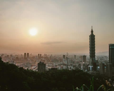 A view of Taipei, capital of Taiwan, from the top of a mountain. The sun is rising over the skyscrapers.