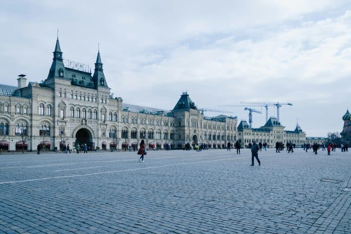 A large square in Moscow, Russia, mostly empty but for a few wandering people. Surrounding the square is a grand building.