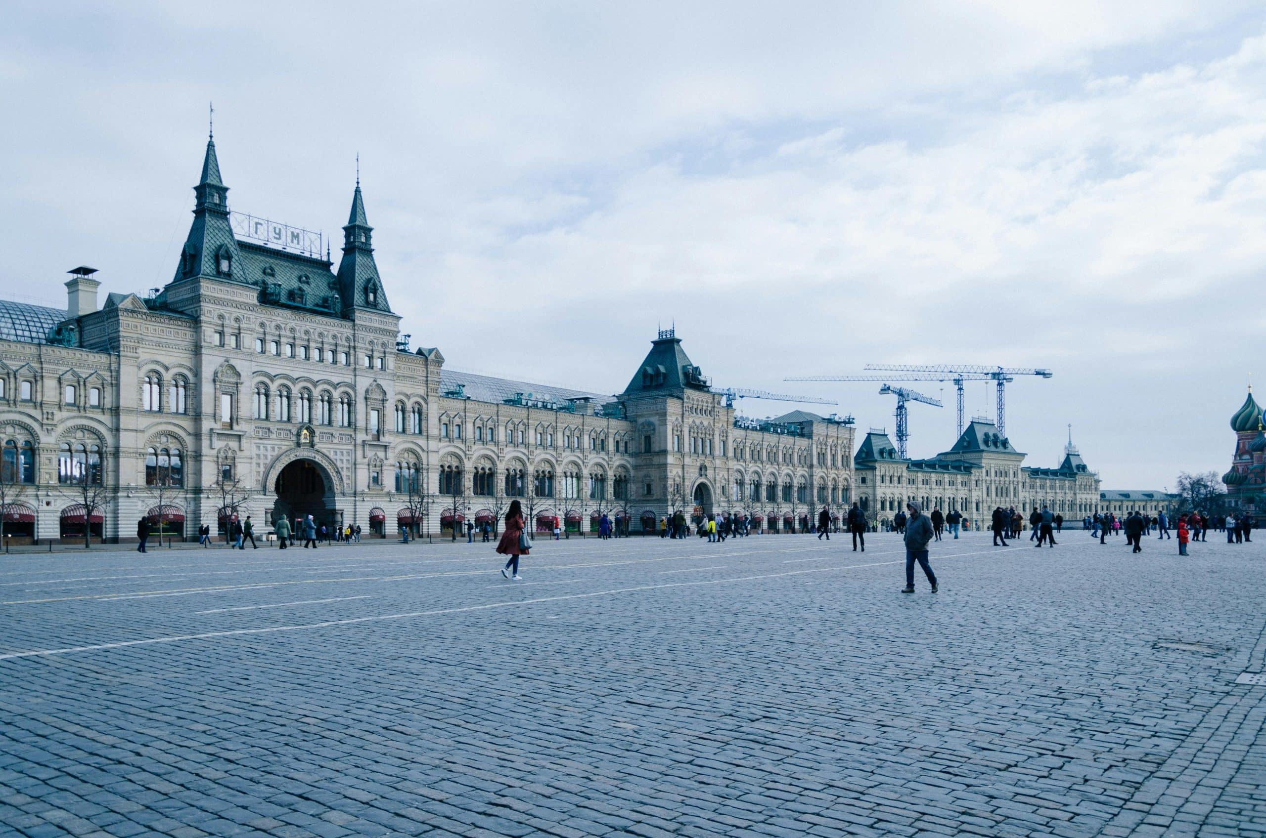 A large square in Moscow, Russia, mostly empty but for a few wandering people. Surrounding the square is a grand building.