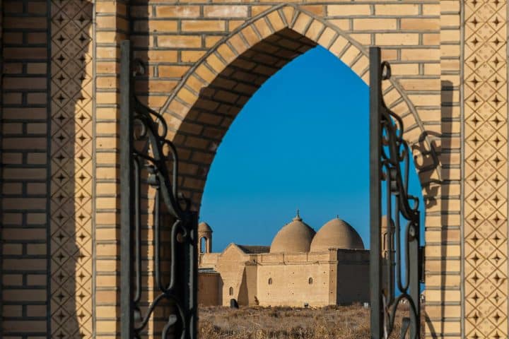 An open gate in a large brick wall shows a glimpse of the Arystanbab Mausoleum in Kazakhstan.