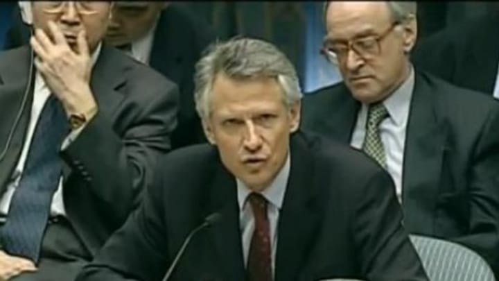 Then French Minister of Foreign Affairs Dominique de Villepin gives his famous speech at the U.N, seated in a dark suit with a red tie. Foreign diplomats sit behind him in several rows as he speaks into a microphone.