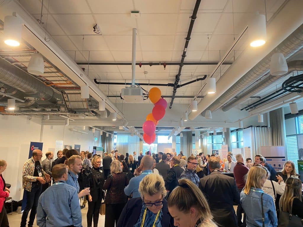 A long room with a large crowd in the middle. On all sides of the room there are banners representing start-up businesses.