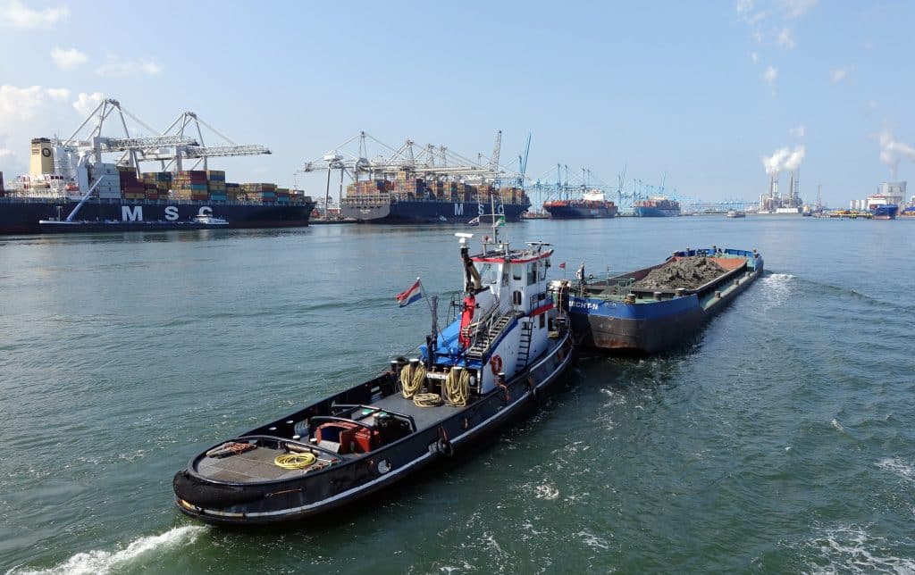 Several large cargo ships are being offloaded in a European harbour, in the Port of Rotterdam. Cranes are seen in the distance.