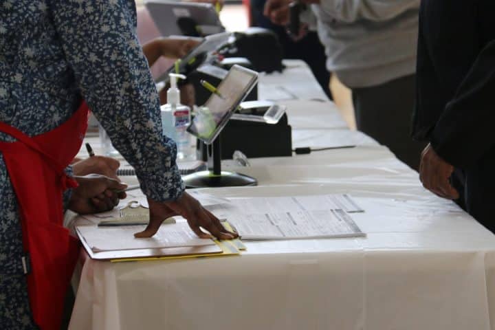 Election workers and voters standing around a table with ballot papers.