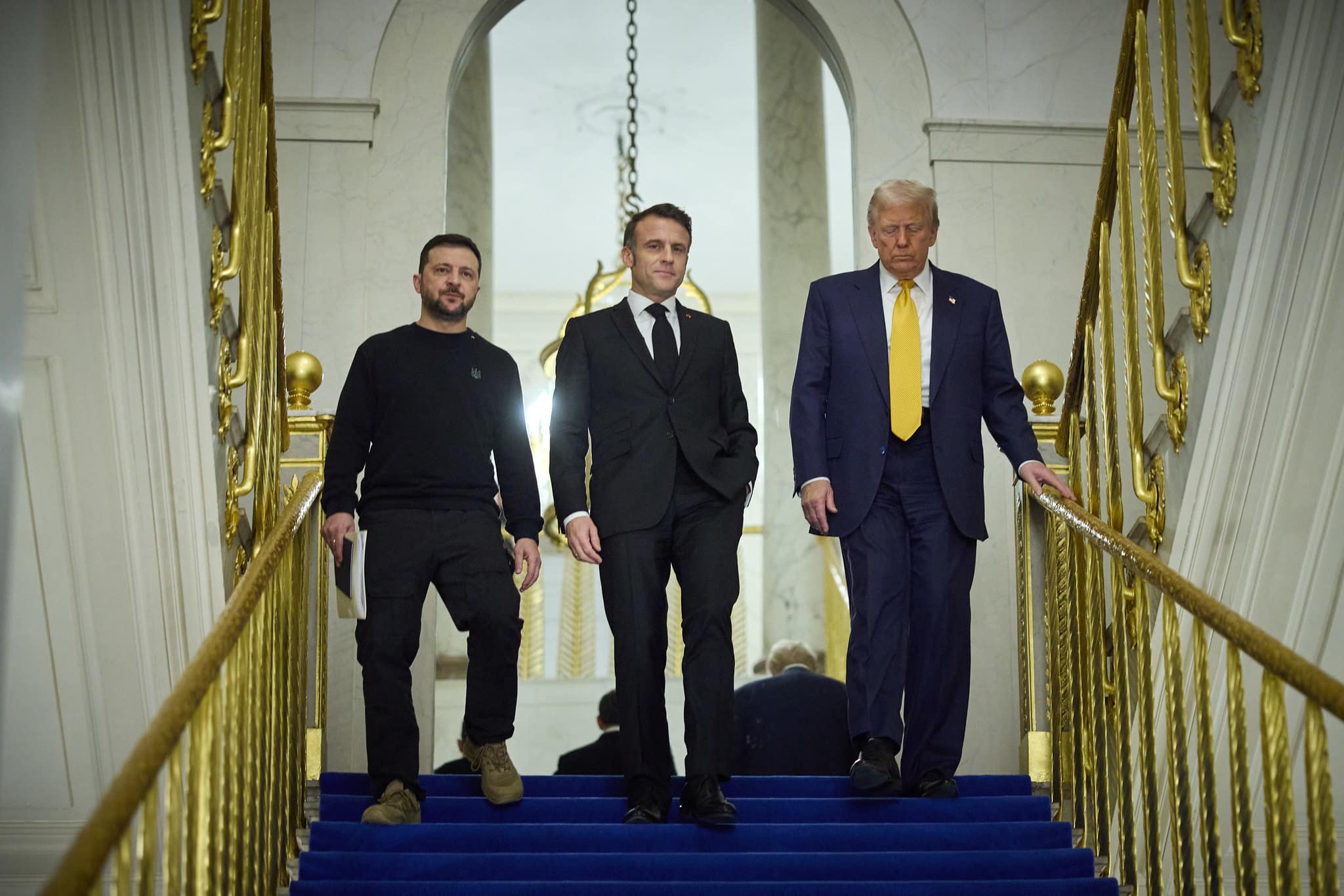 President-elect Donald Trump walking down a staircase alongside President Emmanuel Macron and President Volodymyr Zelenskyy.