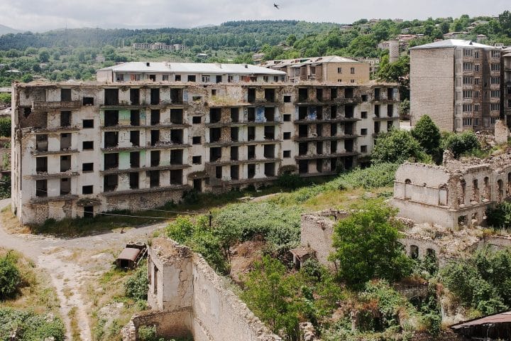 A ruined apartment block in a small city, overgrown with vegetation.