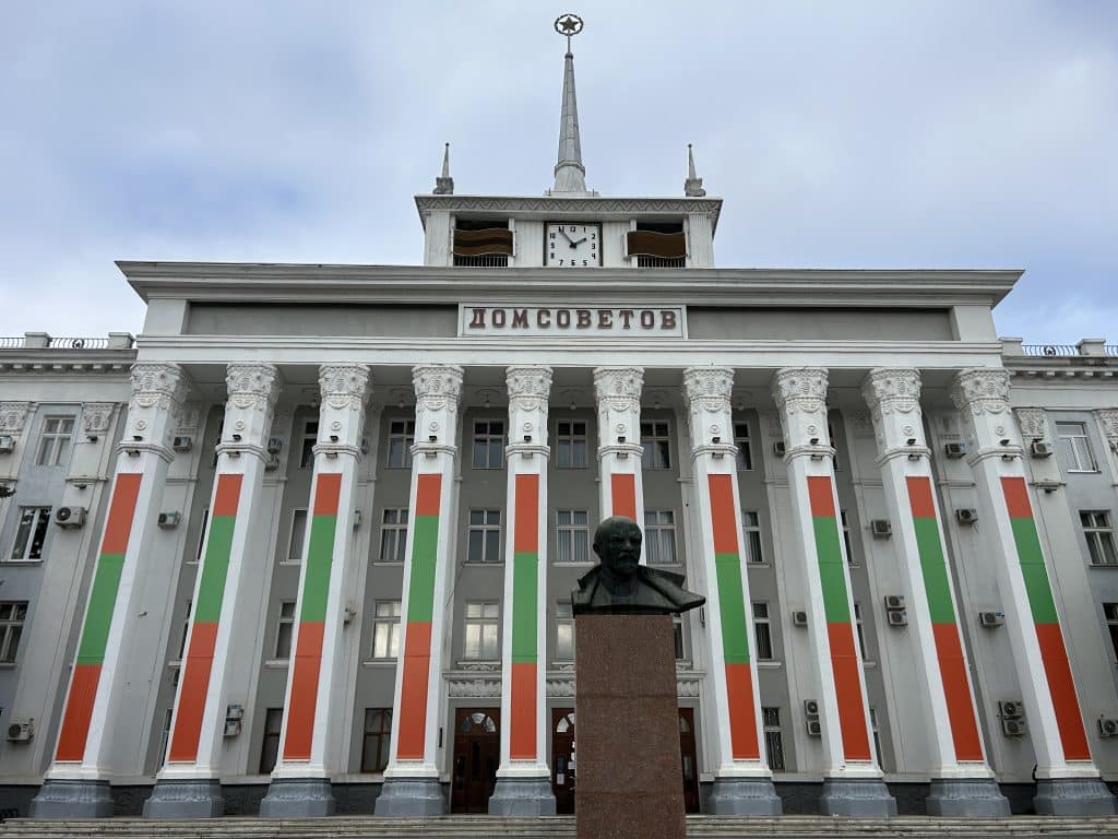 An imposing building with large pillars, with letters reading: "House of the Soviets". In front is a bust of Lenin.