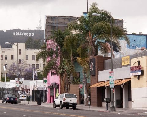 The streets of Los Angeles. Buildings of various colours are seen with the HOLLYWOOD sign in the background.
