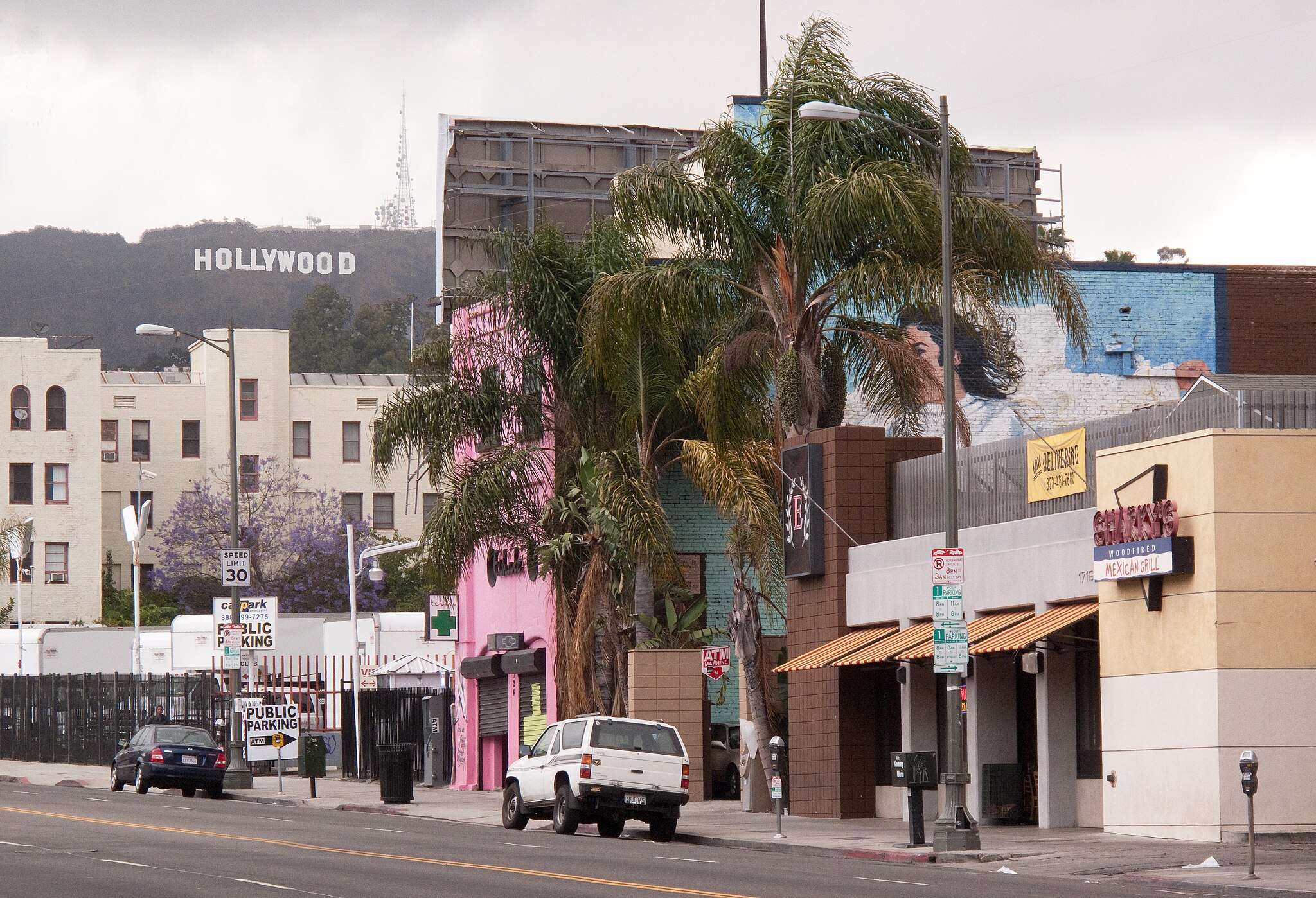 The streets of Los Angeles. Buildings of various colours are seen with the HOLLYWOOD sign in the background.
