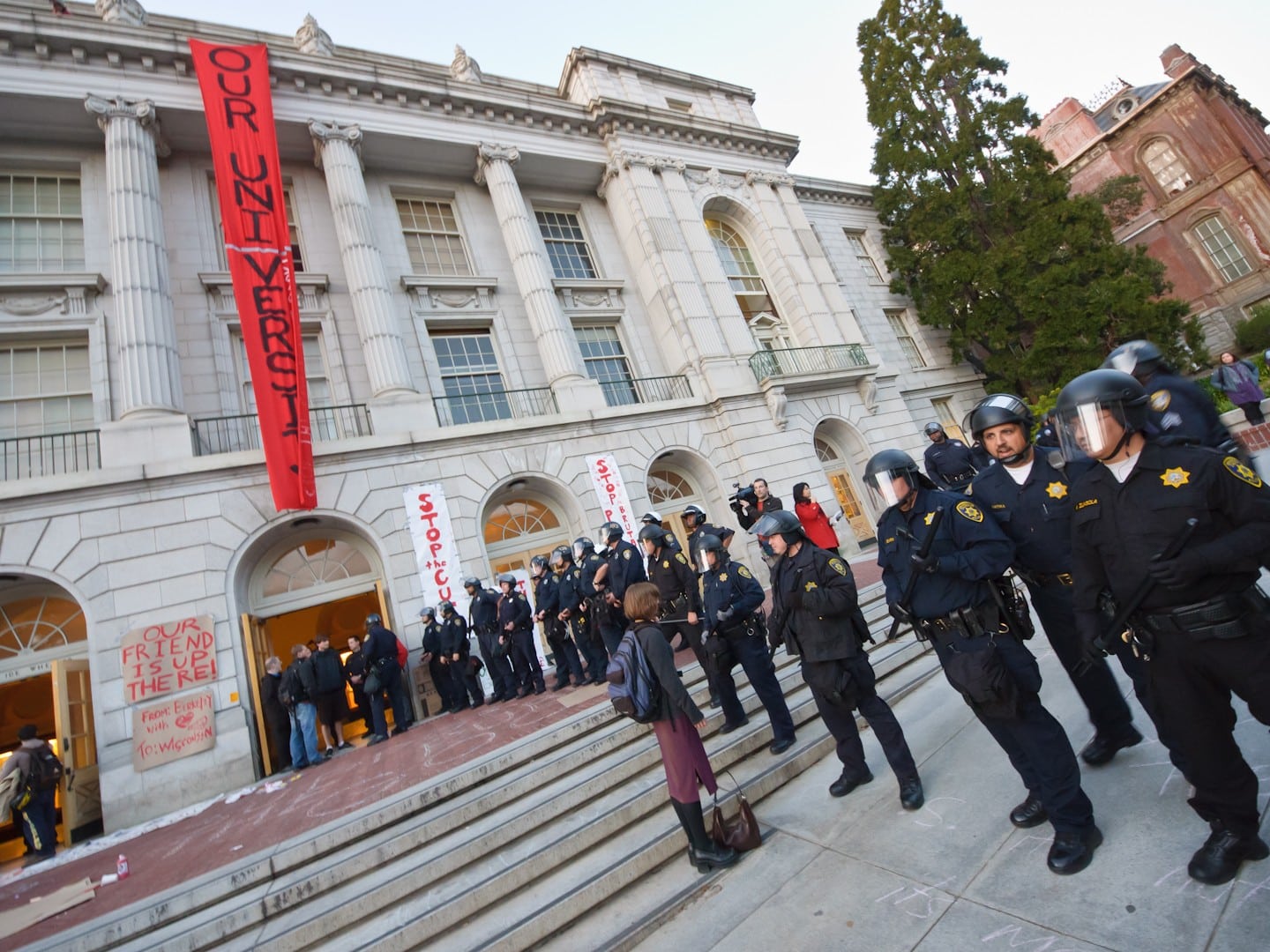 A university building, with police officers in riot gear standing in a line beside it.
