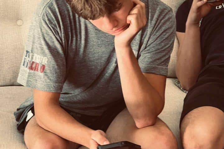 Two young men sitting in a couch, looking at their phones.
