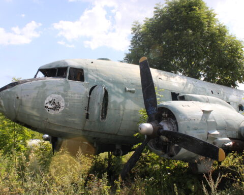 A rusted and derelict plane sitting in an overgrown field.